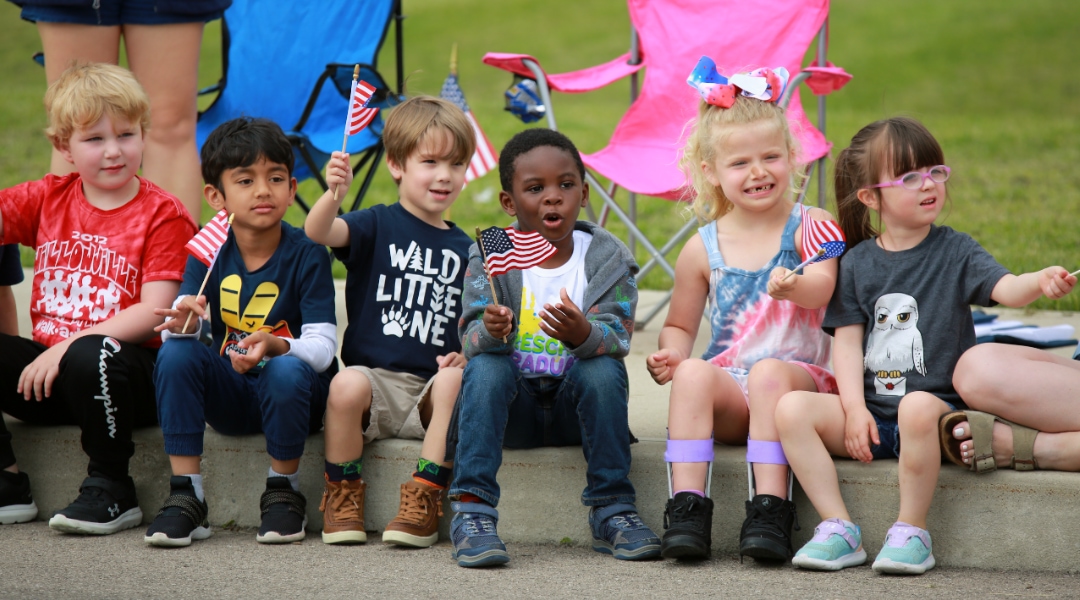 Young students sitting on the curb holding America flags